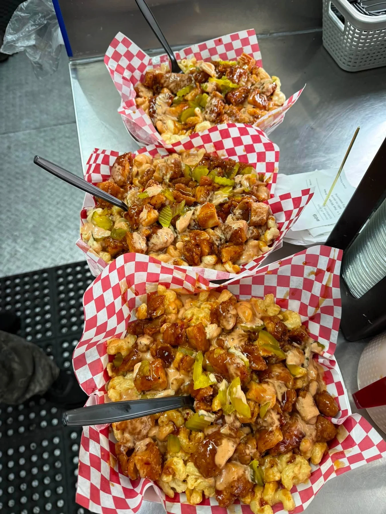 Three trays of loaded macaroni and cheese topped with sauced chicken, pickles, and creamy sauce.